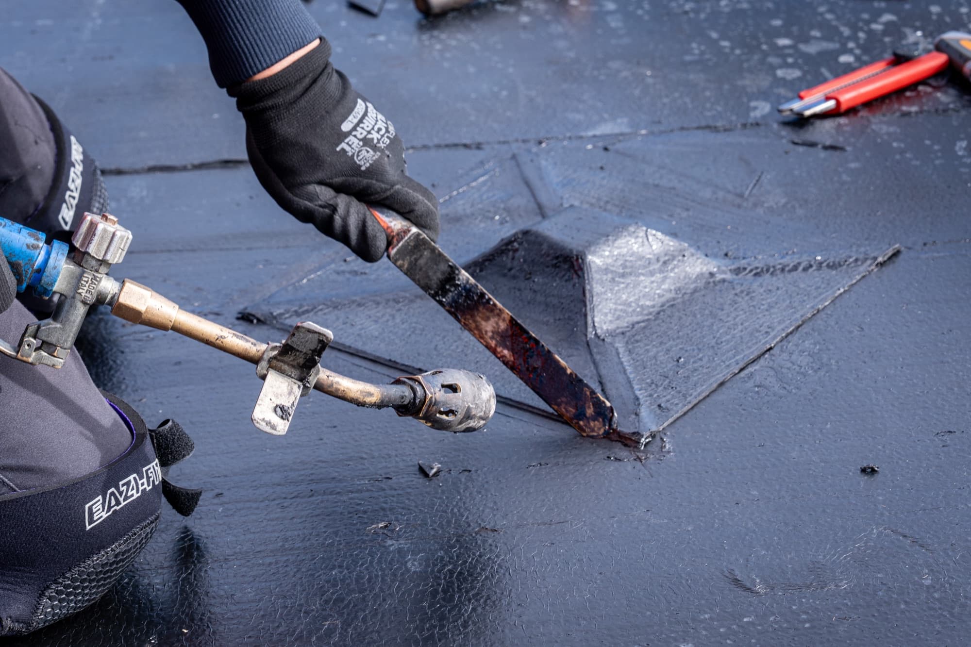 Gloved hands sealing a membrane detail on the roof with a torch and trowel
