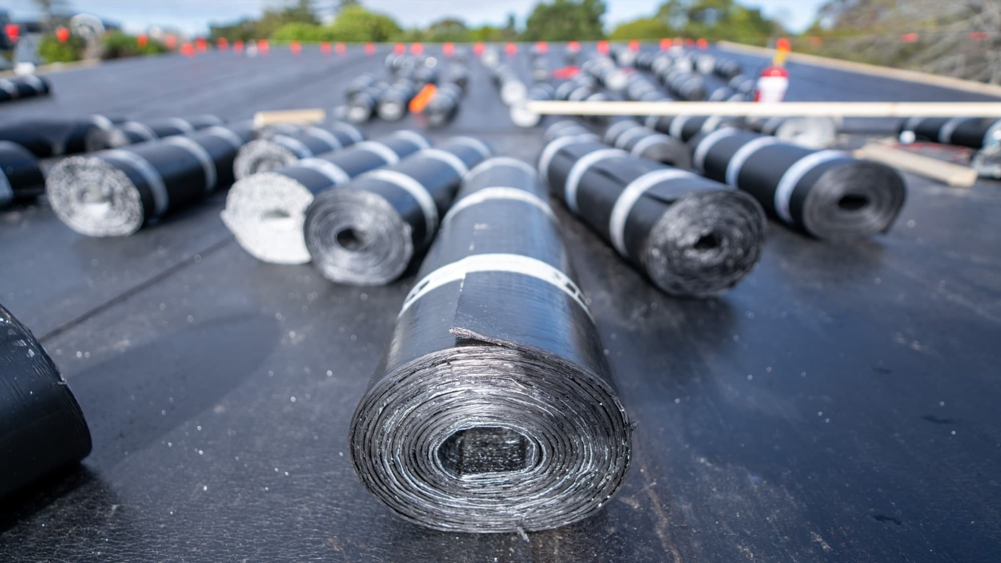 Rows of waterproofing membrane rolls staged across the roof deck ready for installation