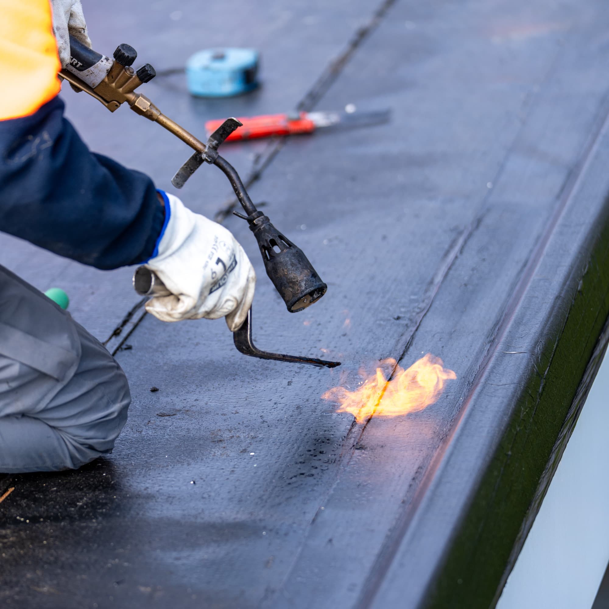 Torch flame bonding a membrane seam alongside the roof edge