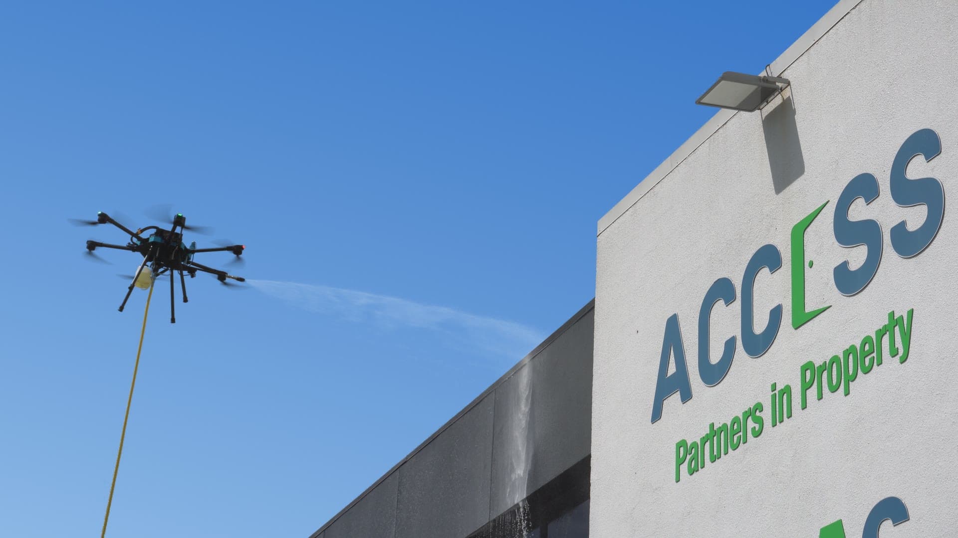 An Access drone spraying water at the Access building, fed by a hose from the ground