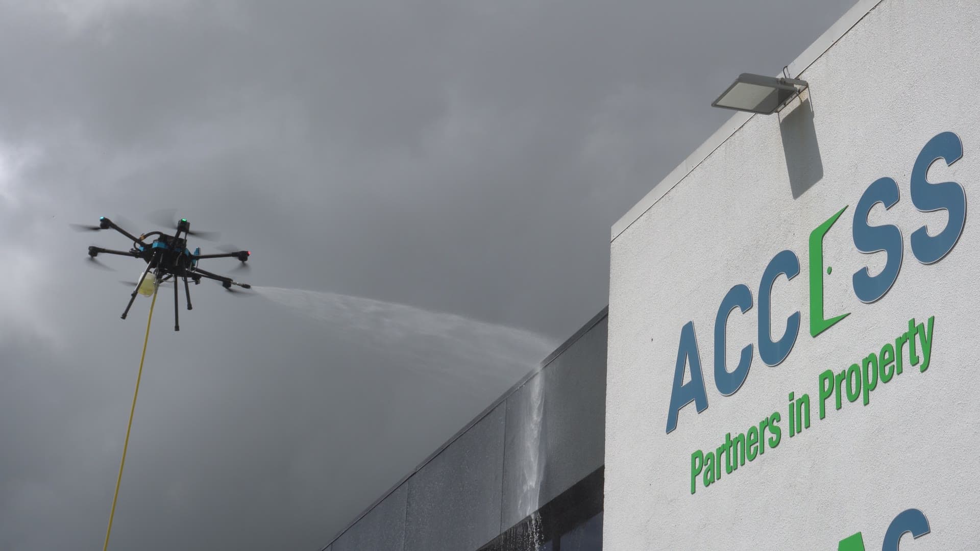 An Access drone spraying water at the Access building, fed by a hose from the ground