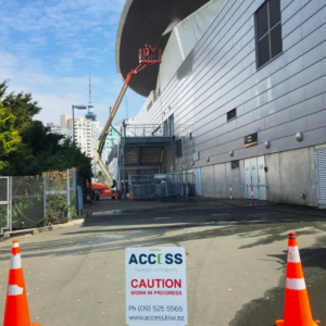 Building maintenance and repair services. Worker on lift cleaning building facade. Caution sign for property maintenance work.