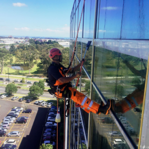 Industrial abseiling: Man cleaning windows at height. Building and property maintenance with rope access.