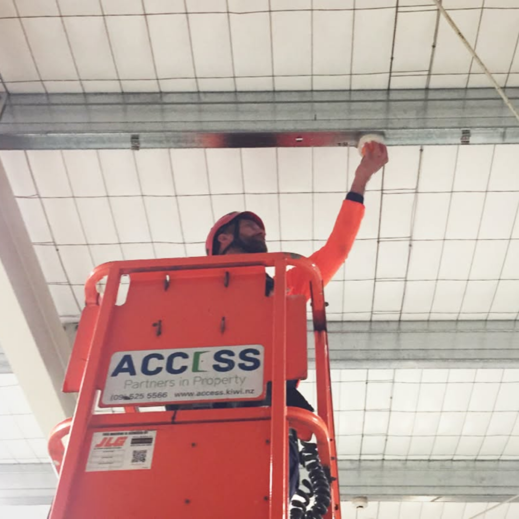 Building maintenance worker on lift performing preventative maintenance on a ceiling fixture. Property maintenance service.